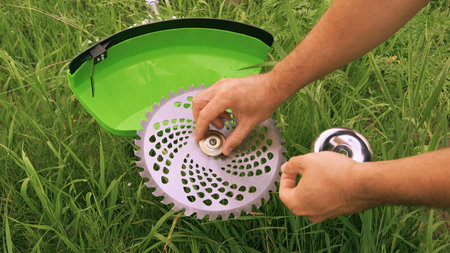 Installing a saw blade on a new green brush cutter. Gardener sets up a saw blade against a grassy...