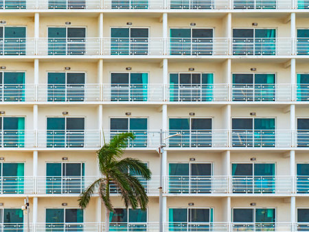 Modern hotel with rows of balconies creates a geometric Pattern, Texture. Green palm tree in front of hotel adds tropical feel. Minimalist design and clean facade emphasize modern travel destinations.の写真素材