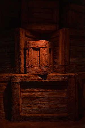 Handmade crate constructed from distressed wood sits in dim light. Gentle warm glow reveals rough surface details. Collection of primitive boxes. Weathered boxes in shadowy underground storageの写真素材