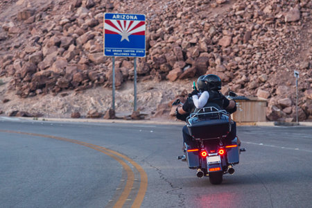 Bikers, man and woman, ride a motorcycle on mountain road and take pictures of sights along way. Two motorcyclists ride customized chopper on winding highway. Rear view, close up.の写真素材