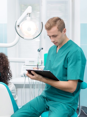 Portrait of a dentist at his dental office with patientの写真素材