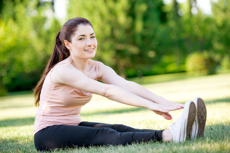 Portrait of a sporty girl doing stretching exercise on the grassの写真素材