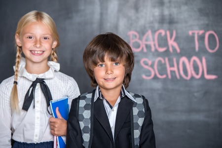 Close-up of happy school boy and girl standing near blackboard with words \"back to school\" on itの写真素材
