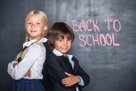 Close-up of happy school boy and girl standing back to back near blackboard with words \"back to school\" on itの写真素材