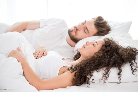 Beautiful young couple sleeping in white bed with window as a background