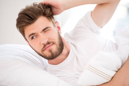 Handsome young man with beard waking up in white bedの写真素材