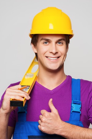 Young smiling repairman in hard hat holding measurement and showing thumb upの写真素材