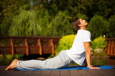 Young man practising yoga and standing in cobra pose with a beautiful green scenery of park on backgroundの写真素材