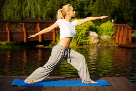 Young blond woman practising yoga with a beautiful green scenery of park on backgroundの写真素材