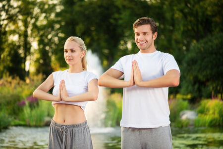 Young happy couple practising yoga with a beautiful green scenery of park on backgroundの写真素材