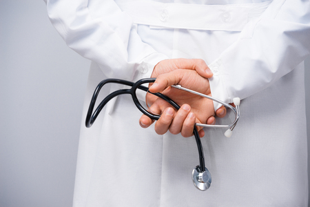 Doctor holding stethoscope behind his back on grey backgroundの写真素材