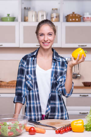 Young pretty smiling woman standing in kitchen and holding yellow paprika. Concept for healthy foodの写真素材