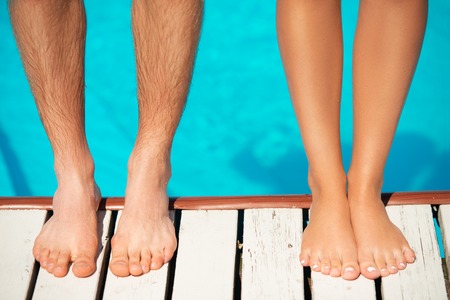 Close-up of beautiful woman and man legs standing near by swimming pool at hot summer dayの写真素材