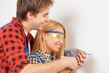 Young smiling repairman helping young woman to learn how to use drillの写真素材