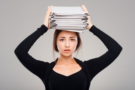 Tired young business woman with a big pile of folders. Concept for overworkingの写真素材