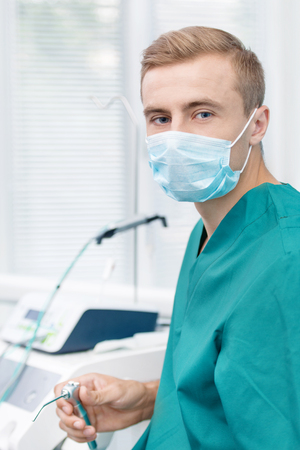 Young dentist in mask holding dental appliance and looking at the cameraの写真素材