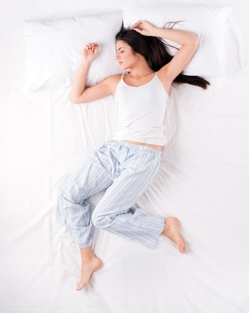 Beautiful young woman sleeping in free fall position on white bed with pillowsの写真素材