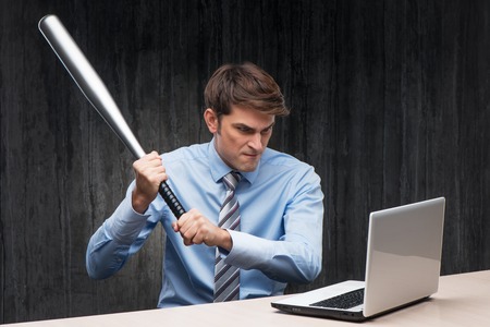 Angry businessman with laptop and throwing-stick. Computer hacker conceptの写真素材