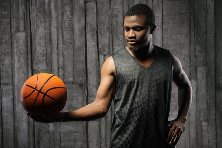 Afro-american young muscular male basketball player holding ball against grunge backgroundの写真素材