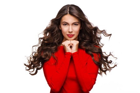 Gorgeous woman with curly hair in red dress looking gently at camera, isolated on white backgroundの写真素材