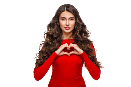 Beautiful young woman with curly hair making heart with hands, isolated on white background. の写真素材
