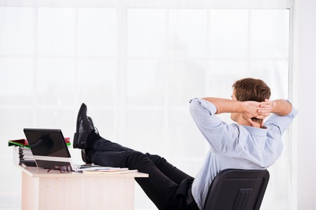 Back side photo of relaxed business man with hands up reposing on headchair. Office big window backgroundの写真素材