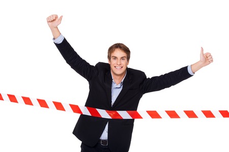 Young smiling businessman crossing finish line with thumbs up. Concept for victory in businessの写真素材