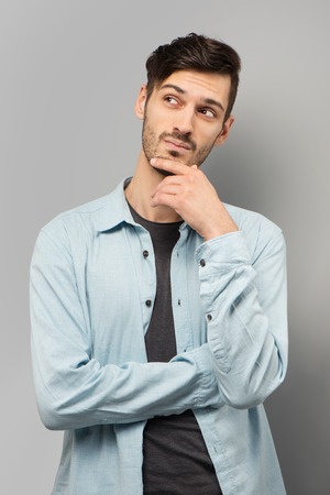 Thoughtful young man looking away, standing on grey backgroundの写真素材