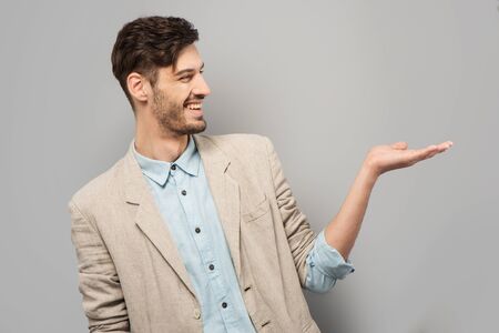 Handsome young man smiling and pointing at something, standing on grey backgroundの写真素材
