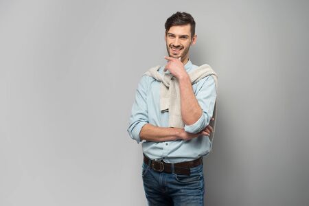 Smiling young man looking at camera, standing on grey backgroundの写真素材