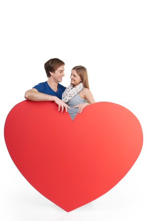 Caucasian couple having romantic time together. Woman and man are behind big red heart. Concept for Valentines Dayの写真素材