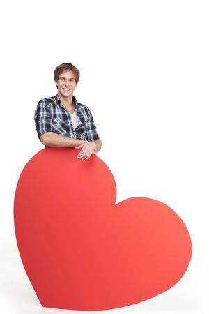 Handsome smiling young man standing behind big red heart and looking at camera. Concept for Valentines Dayの写真素材