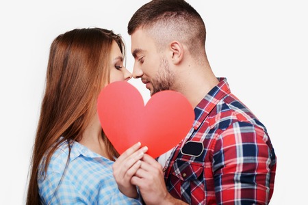 Caucasian couple having romantic time together. Woman and man kissing behind little red heart. Concept for Valentine's Dayの写真素材