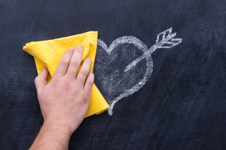 Hand with yellow rag erasing drawing heart from blackboardの写真素材