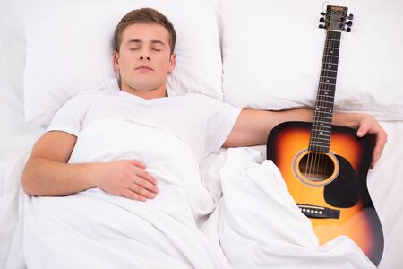Top view photo of handsome young man sleeping and holding guitarの写真素材