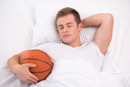 Top view photo of handsome young man. He holding basketball while sleepingの写真素材