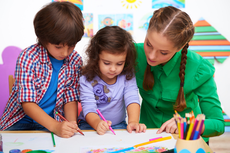 Teacher, little boy and a girl drawing something in preschool center for childrenの写真素材