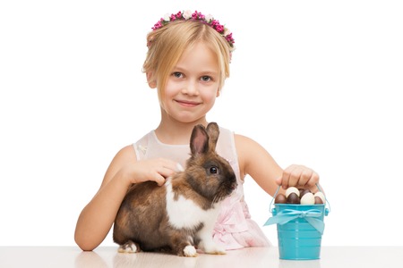 Little smiling girl with cute brown bunny and blue bucket with chocolate eggs, isolated on white backgroundの写真素材
