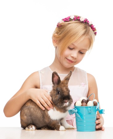 Little smiling girl caressing cute brown bunny and holding bucket with chocolate eggs, isolated on white backgroundの写真素材