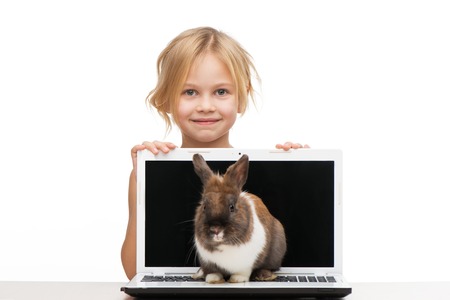 Cute girl looking out of a laptop where little bunny is sitting, isolated on white backgroundの写真素材