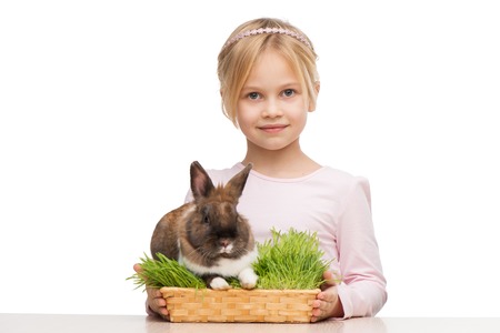 Little girl sitting isolated on white background with cute brown bunny in grassの写真素材