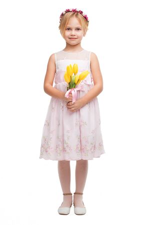 Little girl wearing diadem and pink dress, standing isolated on white background and holding nice bouquet of yellow tulipsの写真素材