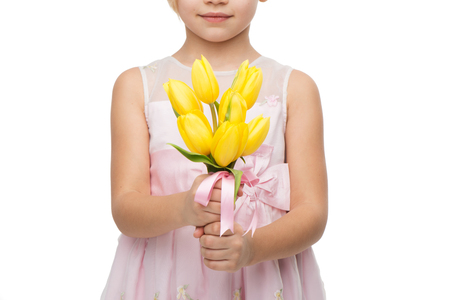 Close up picture of cute girl wearing pink dress, standing isolated on white background and holding nice bouquet of yellow tulipsの写真素材
