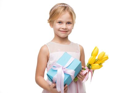 Cute little girl wearing pink dress, standing isolated on white background. Holding nice bouquet of yellow tulips and blue present boxの写真素材