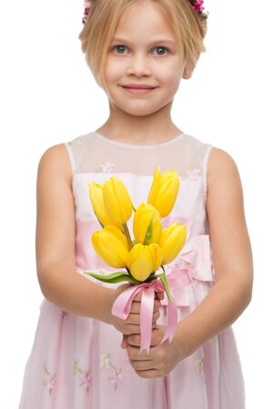 Close up photo of cute girl wearing pink dress, standing isolated on white background and holding nice bouquet of yellow tulipsの写真素材
