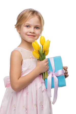 Cute little girl wearing pink dress, standing isolated on white background. Holding nice bouquet of yellow tulips and blue present boxの写真素材