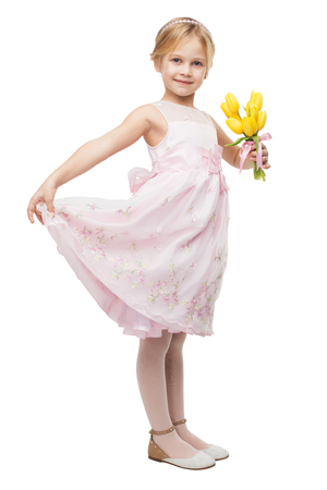 Little girl wearing pink dress, standing isolated on white background and holding nice bouquet of yellow tulipsの写真素材