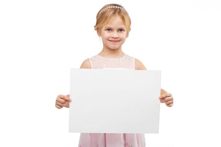 Cute girl wearing pink dress, standing isolated on white background and holding white blank paperの写真素材