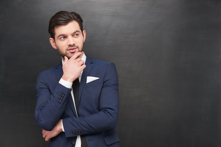 Photo of handsome young thoughtful businessman on blank chalkboard の写真素材