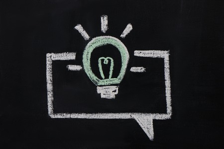 Photo of burning bulb in the dialog box painted with chalk on dark chalkboardの写真素材